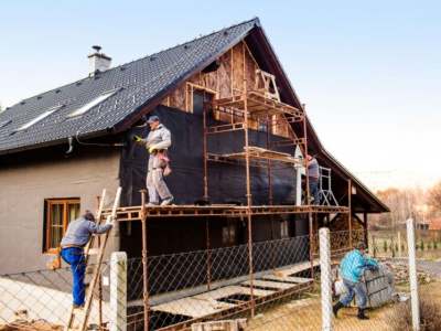 Construction workers thermally insulating house with glass wool